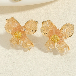 Detailed close-up of golden floral earrings with orange resin petals and crystal centers