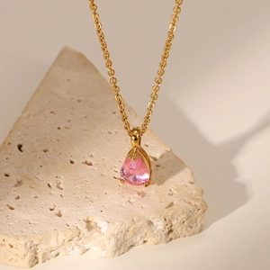 Detail of 18K gold teardrop necklace with pink pear-cut zircon on beige stone stand