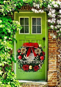 Detail of Christmas wreath with red bow and gold Merry Christmas sign on green door