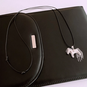 Detail view of silver pony pendant with chain tassels on a black woven cord necklace