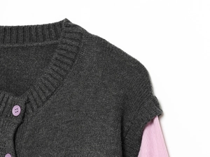 Detail der grauen Rippstrickjacke mit lila Knopf und rosa Lagen-Look-Ärmeln