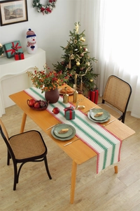 Christmas table runner with red and green stripes and tassels on a wooden dining table
