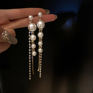Gros plan sur de longues boucles d'oreilles à pompons avec perles et chaînes dorées