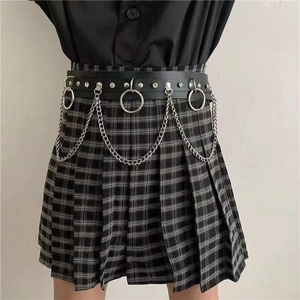 Detail eines Punk-Gürtels mit silbernen Ringen und Kette auf grauem Karorock
