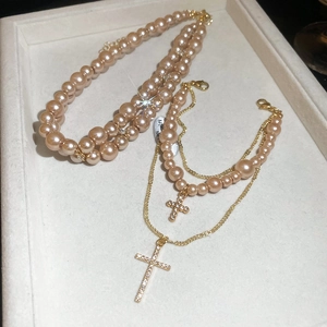Close-up of champagne pearl necklace layered with rhinestone cross pendant on velvet tray