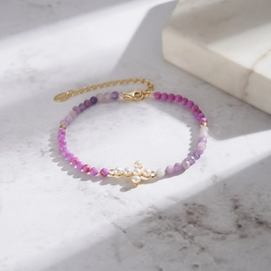 Macro detail of purple bead bracelet featuring a white freshwater pearl cross charm