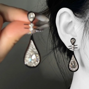 Detailed close-up of teardrop-shaped rhinestone earrings with black plating and silver pins