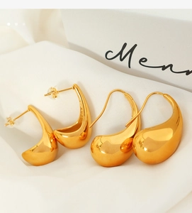 Macro shot of gold teardrop earrings in stud and hook styles on a soft fabric