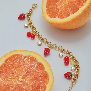 Detail of gold strawberry and cherry pendant bracelet with sparkling crystals on orange