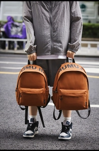 Outdoor shot of caramel nylon backpacks with letter prints and large front zip pockets