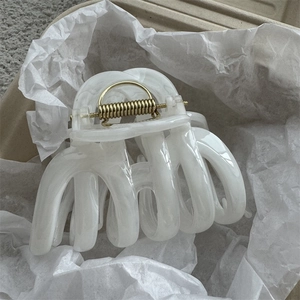 Close-up of white ink-marble resin hair claw clip resting on white tissue paper