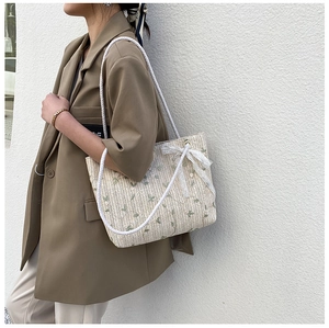 Detail of hand-woven straw tote with white rope handles and delicate lace bow accent