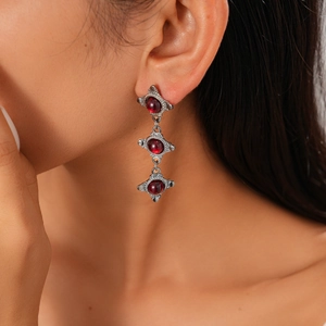Close-up of vintage silver drop earrings with three tiered dark red resin gemstones