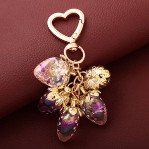 Detailed view of strawberry bag charms with golden heart clasps on leather background