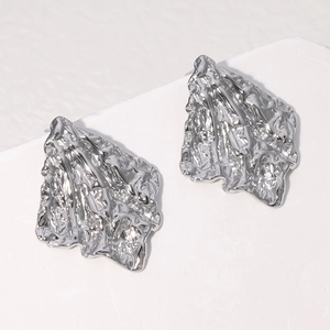 Détail macro de boucles d'oreilles en métal argenté irrégulier avec texture fondue