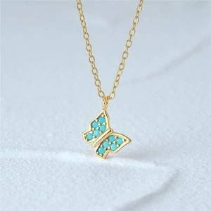Detail of a gold butterfly pendant necklace with turquoise beads on a textured surface