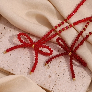 Red faceted crystal bead bow necklace with gold accents on elegant silk fabric