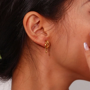 Close-up of golden fluid-style earrings with polished finish on a model's ear