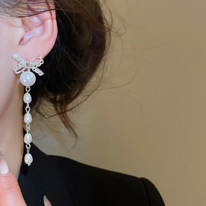 Detailed close-up of silver bow earrings featuring sparkling stones and pearl tassels