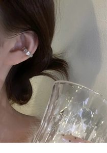 Détail d'un ear cuff argenté avec zircone carrée porté sur l'oreille d'une femme