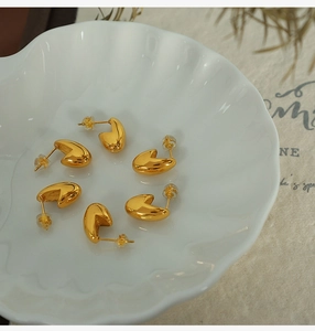 Macro view of gold bean stud earrings with polished finish on a ceramic shell dish