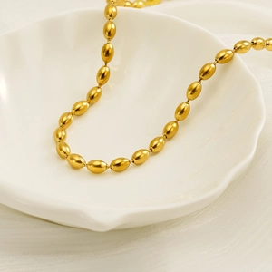Detailed view of golden oval rice bead necklace displayed on a white shell ceramic plate