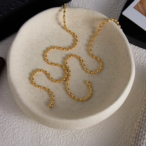 Close-up of 18K gold stainless steel rice bead Y-necklace on a ceramic tray