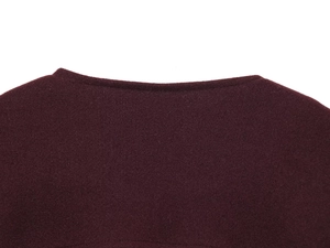 Detailansicht des Rundhalsausschnitts einer burgunderroten Wolljacke mit Goldknopf