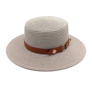 Detail of woven straw hat featuring a brown leather band and gold decorative buckles