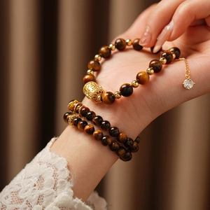 Detailed view of tiger eye stone bracelet with gold beads and zircon charm on model wrist