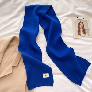 Detailed texture of a soft blue knitted scarf with a small woven label on a lifestyle set