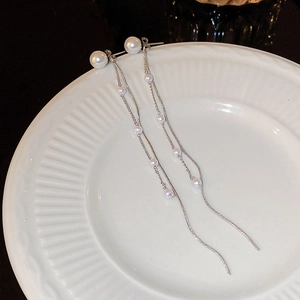Detailed view of silver tassel earrings with white pearls hanging on a white porcelain dish