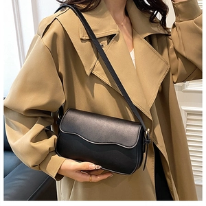 Fashionable black leather shoulder bag styled with a khaki trench coat on a model