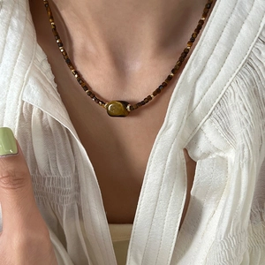 Detailed view of beaded necklace with tiger eye stone on white V-neck garment