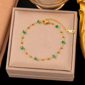 Detail of a gold stainless steel bracelet with green heart beads in a beige jewelry box