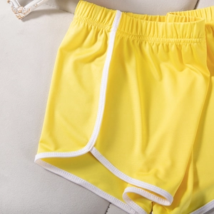 Detail shot of yellow sports shorts featuring white piping and elastic waistband