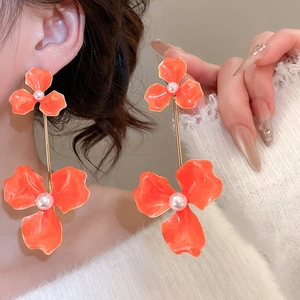 Macro detail of large orange floral earrings with pearl center and golden drops