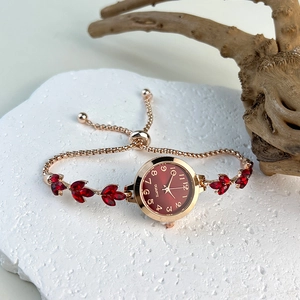 Detail of rose gold quartz watch with red leaf-shaped gems and brown dial on a white stone