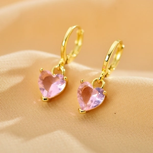 Close-up of gold earrings with pink heart gemstones on luxury gold silk background