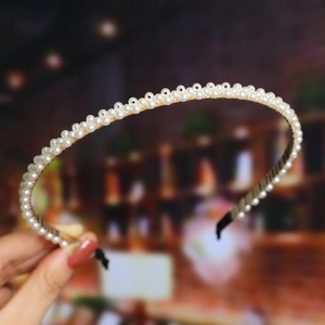 Detail of a thin gold metal headband featuring white pearls held by a hand