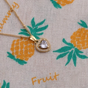 Collier à pendentif cœur doré avec pierres en zircon sur un fond décoratif à motifs de fruits