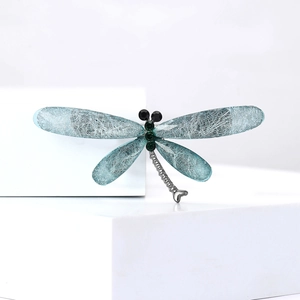 Detailed view of dragonfly brooch with blue silk-textured wings and green crystal body