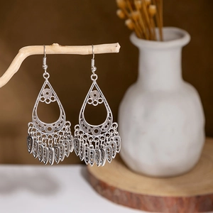 Close-up of vintage hollow silver earrings with water-drop tassels on a wooden branch