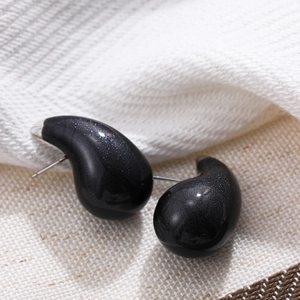 Detail of black glitter teardrop earrings on white fabric with silver metal studs