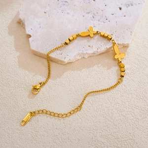 Bracelet papillon en acier inoxydable doré avec perles cubes sur socle marbre
