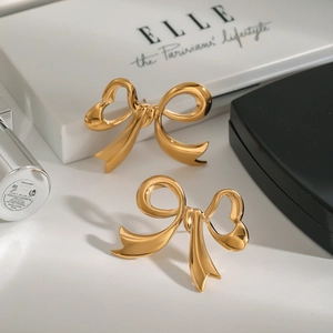 Elegant gold bow earrings in polished titanium steel on a luxury jewelry display