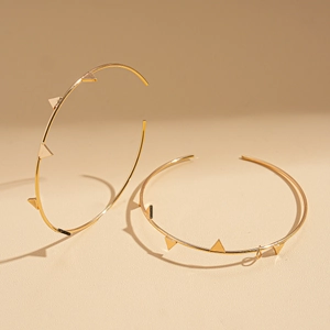 Detailed close-up of golden geometric hoop earrings with triangle stud accents in warm lighting
