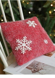 Detail of red plush Christmas pillow with white snowflake patches on a white chair