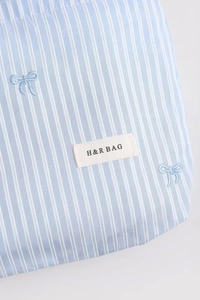 Détail de la broderie noeud à carreaux bleus et étiquette H&R BAG sur la trousse