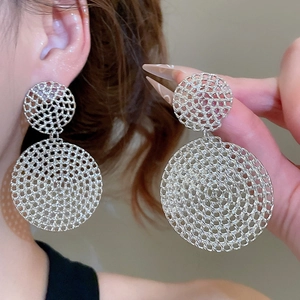 Close-up of silver hollow spiral mesh earrings showing intricate woven metal detail